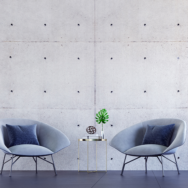 Two gray lounge chairs with navy cushions beside a gold side table against a concrete wall.