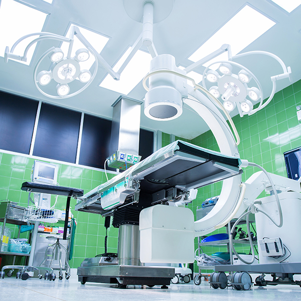 Operating room with a surgical table, overhead lights, imaging equipment, and green tiled walls.